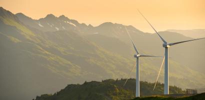 Two wind turbines on the side of a mountain with yellow sky behind