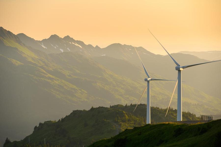 Two wind turbines on the side of a mountain with yellow sky behind